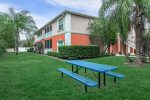 Exterior view of Harvard Condominiums featuring green lawn, picnic table, and colorful building in Melbourne, Florida.