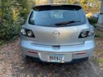 Rear view of a 2007 Mazda 3 hatchback parked in a driveway, showing license plate and features.