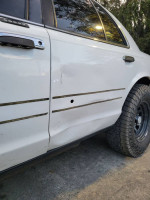 Side view of a 2001 Crown Victoria with a dent and custom lift, showcasing unique tire and body modifications.