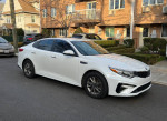 2019 Kia Optima LX sedan in pearl white, parked on a street, showcasing its sleek design.