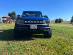 Front view of a blue 2022 Ford Bronco Big Bend with new tires and lift on grass