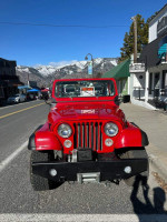 Front view of a red 1976 Jeep CJ7 for sale, showcasing its off-road features and scenic background.