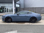 2024 Ford Mustang GT Premium in gray, side view, parked outside a dealership with modern architecture.