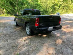 Rear view of a black 2003 Chevrolet Silverado 1500 SS parked in nature with lush greenery.