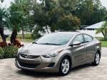 2012 Hyundai Elantra in excellent condition with grey-brown metallic finish parked amidst lush greenery