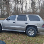 Silver 2000 Dodge Durango SLT parked in a wooded area, showcasing new tires and third-row seating.