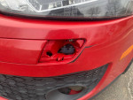Close-up of a red Volkswagen Jetta's damaged headlight area showing minor scratches and missing components.