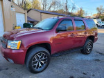 2007 Chevrolet Tahoe LTZ in red, showcasing its sleek design and new tires, parked outside.