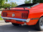 Rear view of a classic 1969 Ford Mustang Mach 1 in Calypso Coral color parked outdoors.
