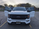 Front view of a 2023 Ford F150 FX4 Hybrid truck with opened doors in a parking lot.