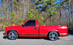 1989 Chevrolet C1500 Silverado Pickup in red with chrome wheels, parked in a natural setting