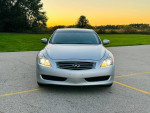 Front view of a 2009 INFINITI G37X AWD Coupe with sunset background, showcasing its sleek design and headlights.
