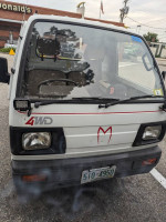 Front view of a 1989 Mazda Scrum KEI truck with 4WD, parked in a lot with a McDonald's in the background.