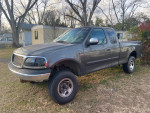 2002 Ford F150 truck with minor lift, needing repairs, parked in grassy area.