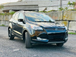 2016 Ford Escape Titanium FWD parked in a clean urban area, showcasing its sleek design and black alloy wheels.