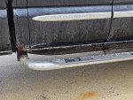 Close-up view of the rusted rocker panels of a 2005 GMC 2500 SLT truck with chrome step rail.