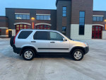 2002 Honda CR-V in silver with manual AWD, new tires and clean interior, parked in front of a modern building.