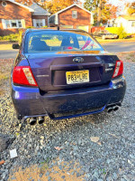 Rear view of a 2013 Subaru Impreza WRX with aftermarket exhaust on gravel driveway