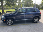 2015 Volkswagen Tiguan SE 4Motion AWD parked, featuring leather interior and roof rack in a sunny outdoor setting.