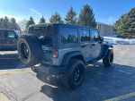 2014 Jeep Wrangler in Anvil gray with lifted suspension and aftermarket wheels, parked in sunny lot.
