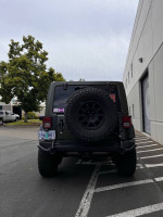 Rear view of a well-maintained 2015 Jeep Wrangler Rubicon in Tank Green, parked in a lot.