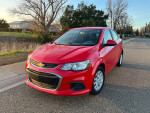 Front view of a red 2018 Chevrolet Sonic LT parked on the street, showcasing its sleek design and efficient structure.