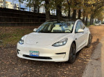 2021 Tesla Model 3 with full self-driving, parked in a scenic outdoor setting, showcasing its sleek design and white exterior.