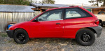1998 Chevrolet Metro hatchback with 100,000 miles, in red, parked outdoors on gravel