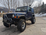 2000 Jeep Wrangler Sport 4WD in blue color parked in a scenic outdoor area, showcasing its rugged design.
