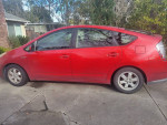 Red 2006 Toyota Prius with black leather seats, parking in a driveway, showcasing its hybrid design.