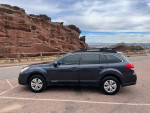 Side view of a 2013 Subaru Outback parked in front of rocky terrain, ideal for adventure and outdoor exploration.