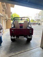 Rear view of a red 1973 Jeep CJ5 parked, showcasing its new tires and interior details.