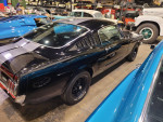 1965 Ford Mustang Fastback in Raven Black with charcoal stripes, showcasing its sleek design in a restoration garage.