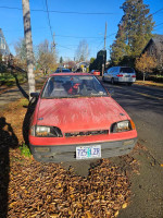 Front view of a red 1990 Geo Metro parked on a leaf-covered street, showcasing its salvage title and vintage design.