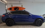 Side view of a lifted blue Mercedes-Benz GLC Coupe in a garage, showcasing its sleek design and new all-terrain tires.