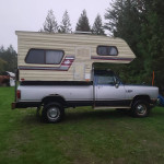 1989 Dodge Ram W250 4x4 with camper shell parked on grass, showcasing classic design and details.