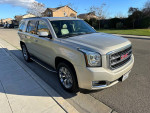 2015 GMC Yukon SLT RWD parked on the street, showcasing its sleek design and alloy wheels.